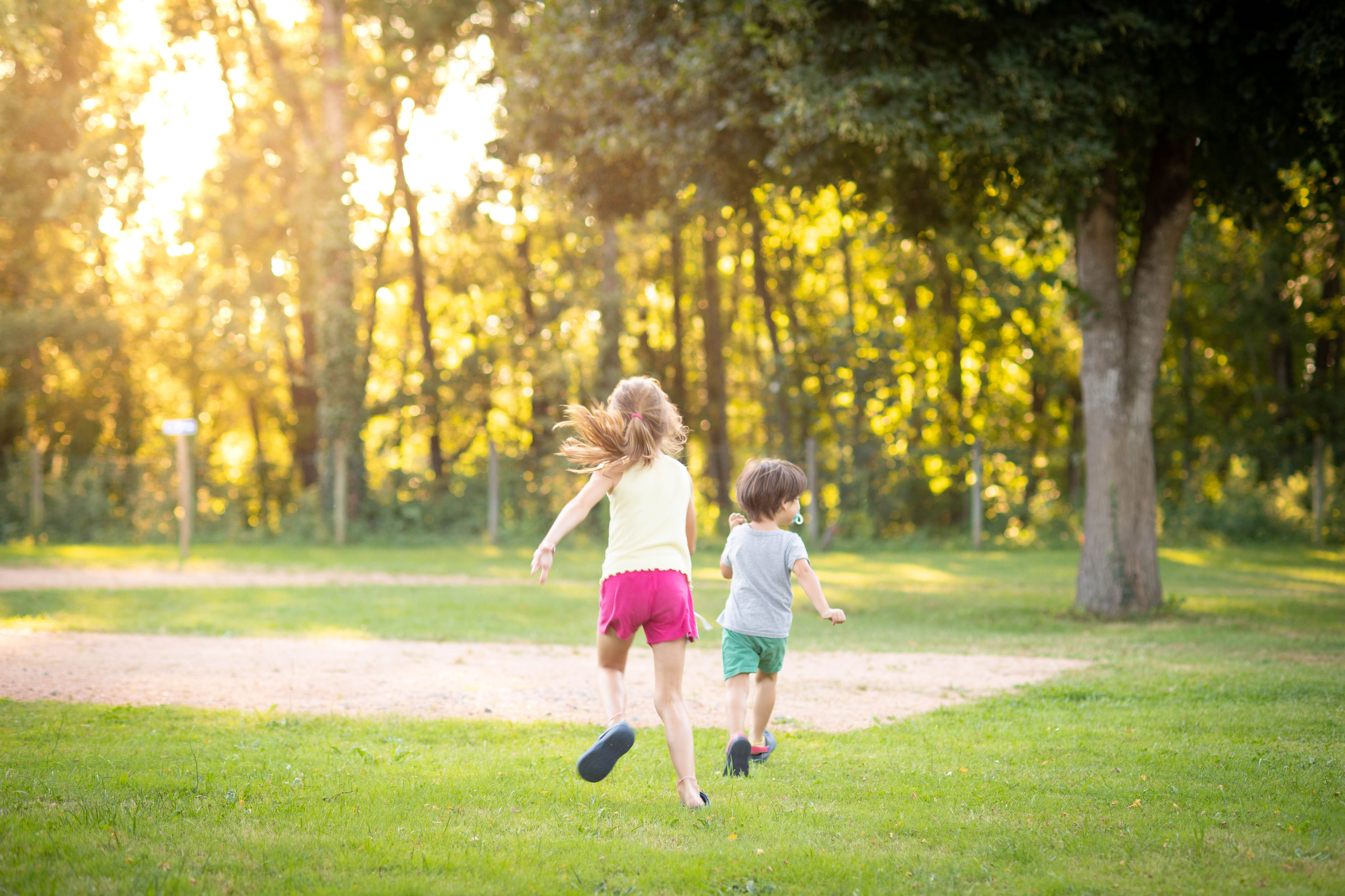 Two children running joyfully across a grassy park with trees in the background, depicting freedom and happiness in an outdoor setting