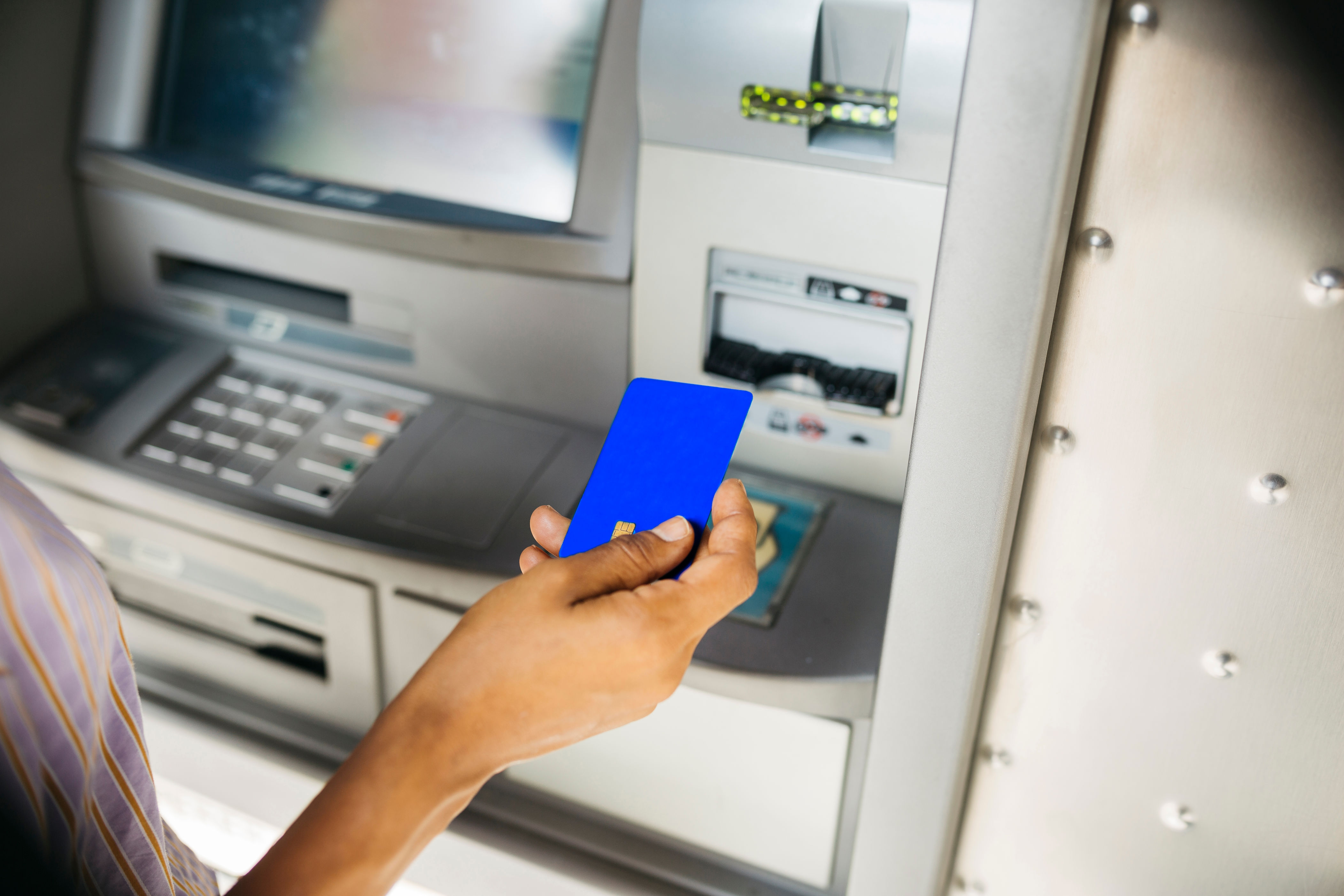 Person holding a card near an ATM, ready to insert it for a transaction