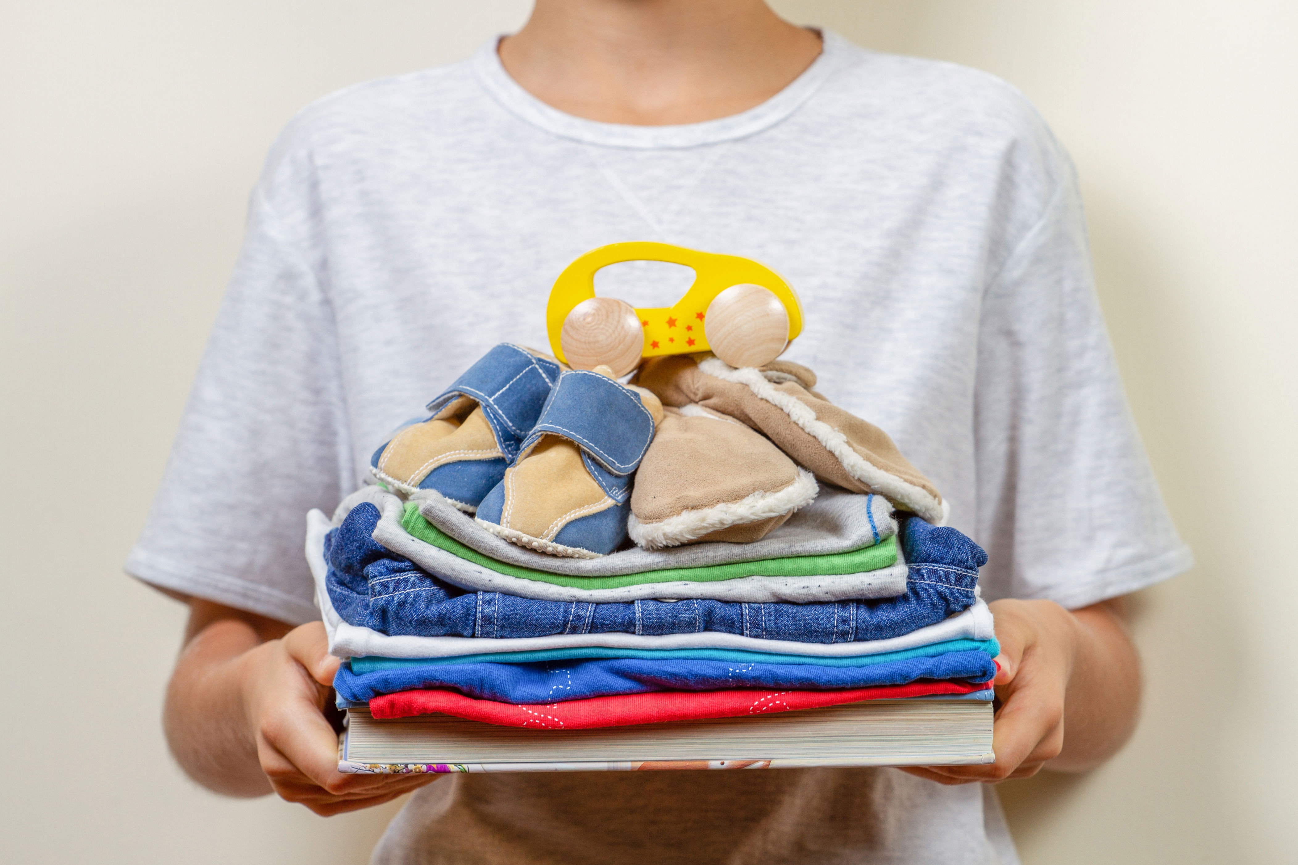 Person holding a stack of folded baby clothes and shoes on a small box, suggesting organization and preparation for parenting or gift-giving