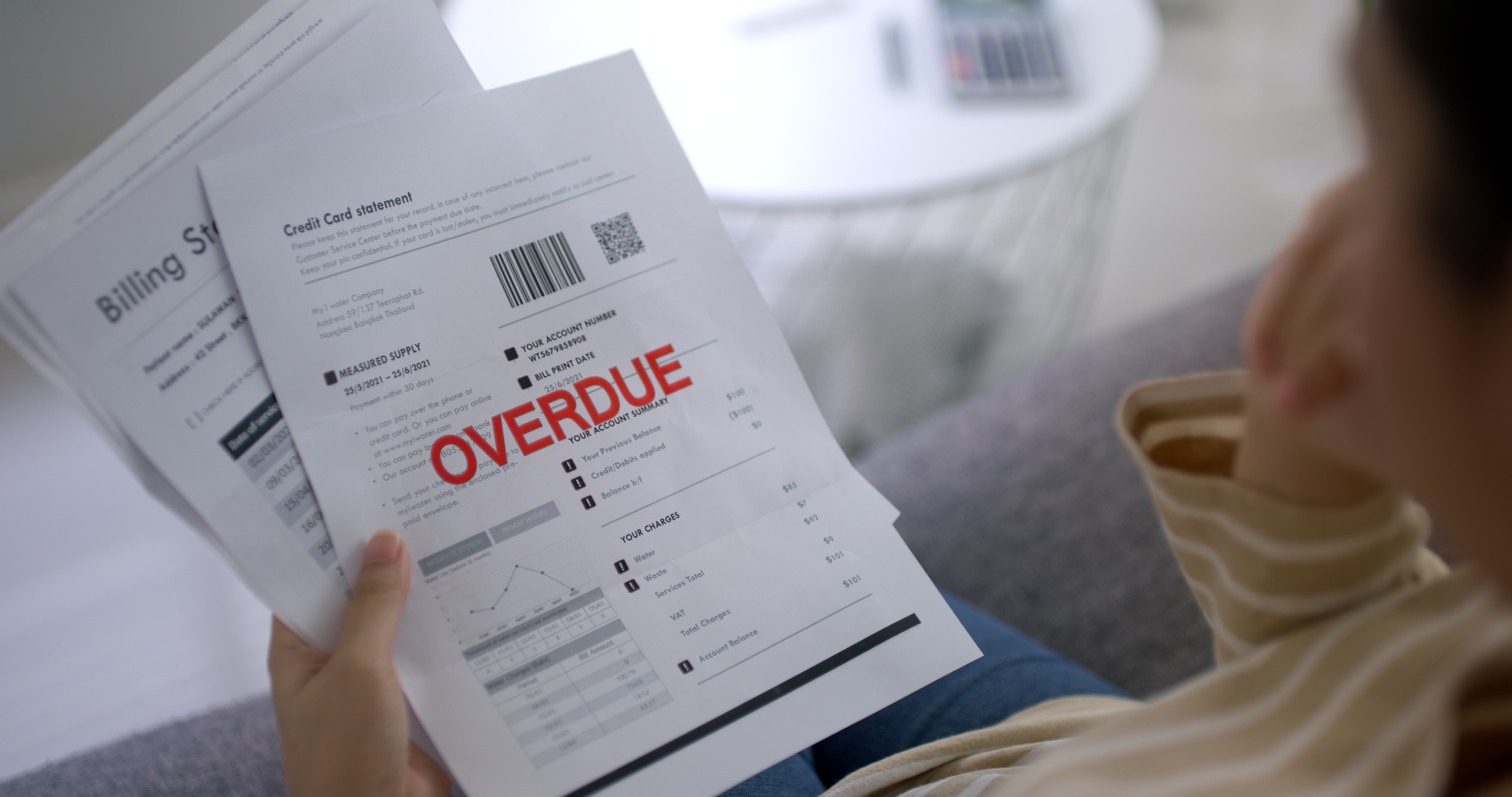 Person viewing a credit card statement marked "OVERDUE" while sitting on a couch, highlighting financial stress