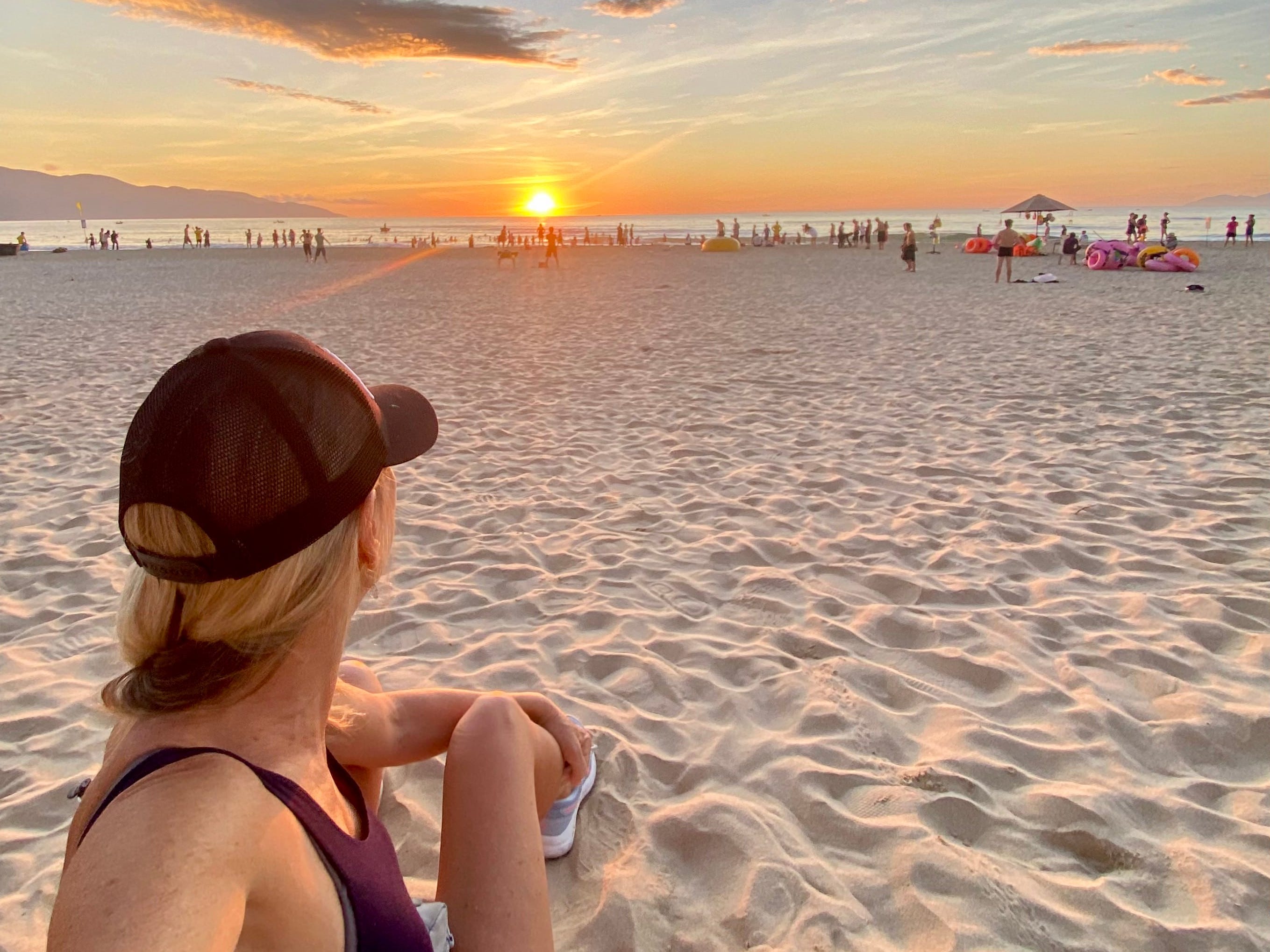 A woman taking a photo of herself on the beach watching the sunrise.