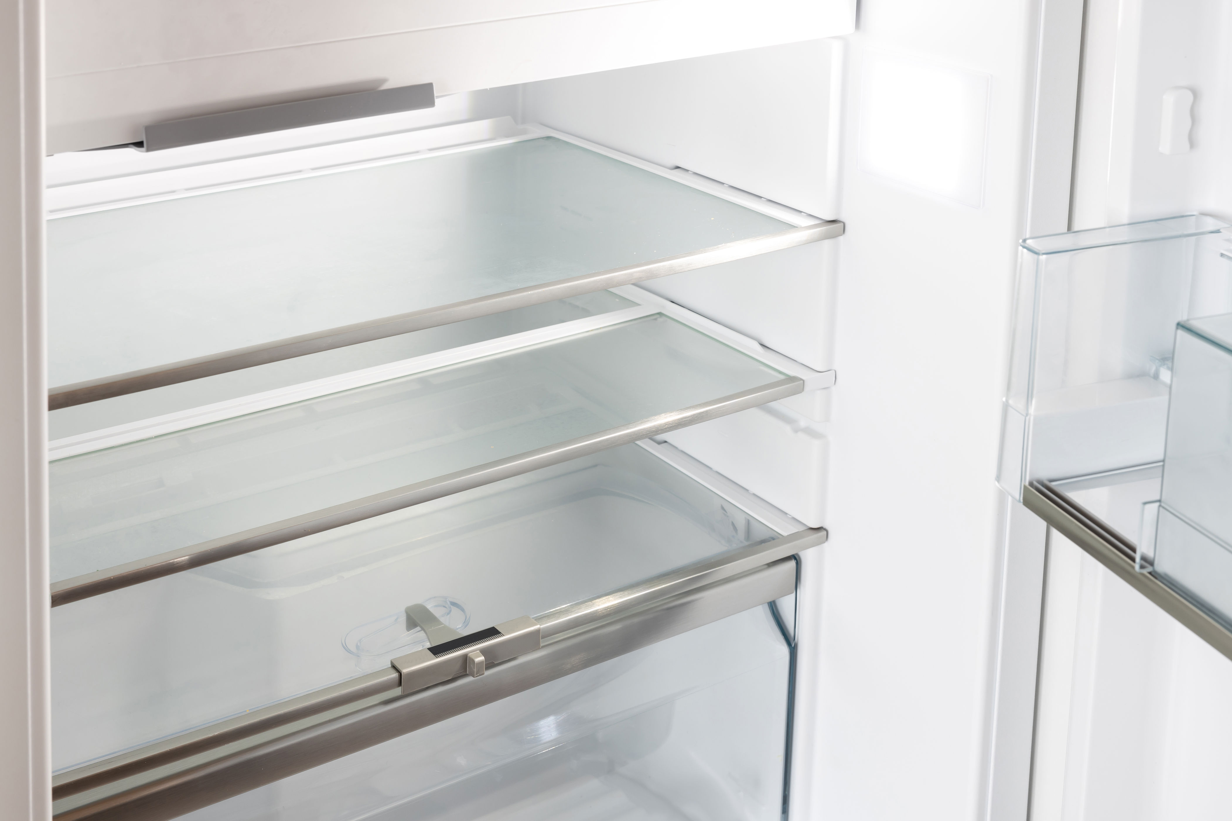 Open, empty refrigerator with glass shelves and a transparent crisper drawer