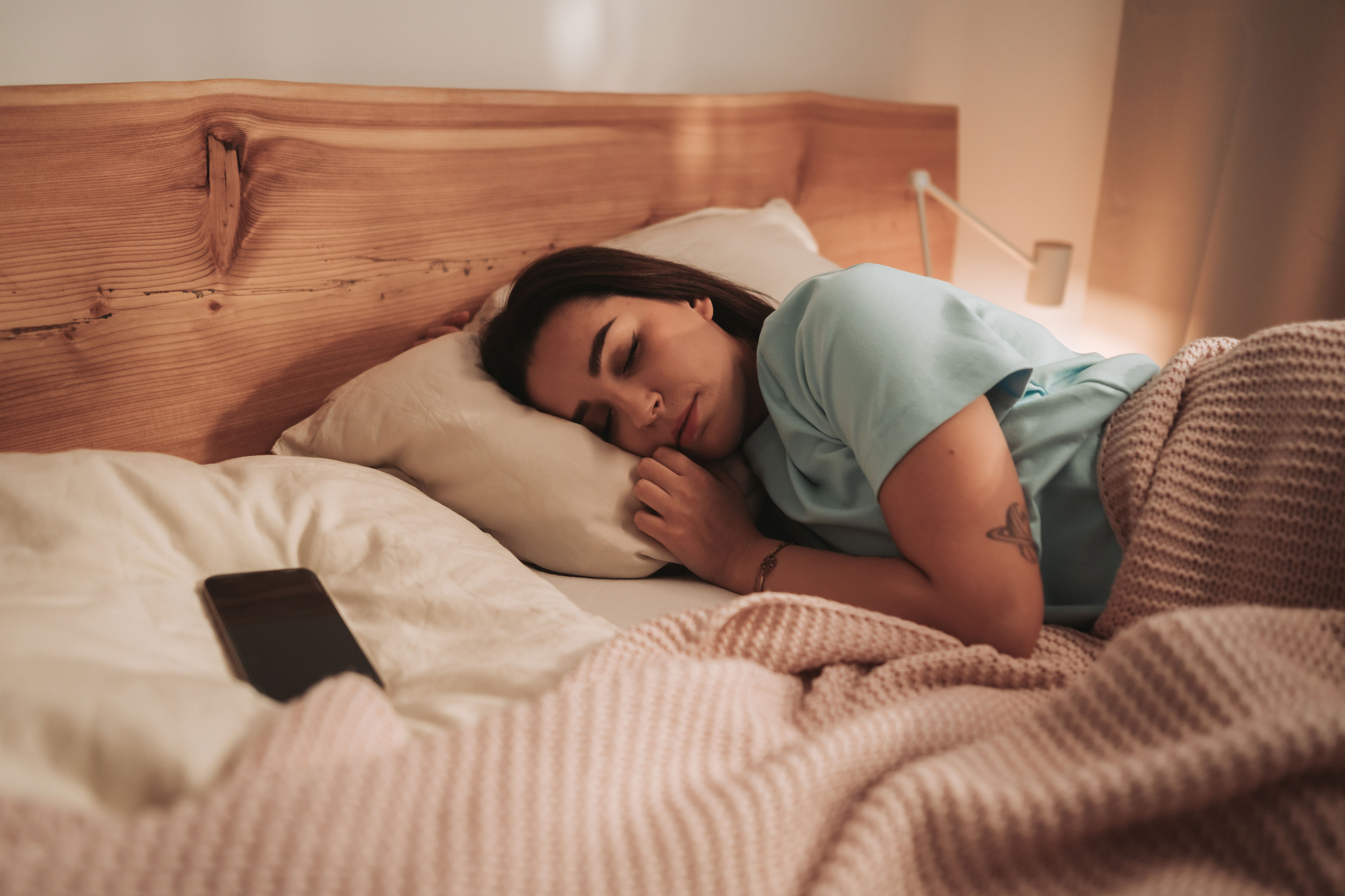 Person sleeping in bed, resting on a pillow with a smartphone nearby. Cozy atmosphere