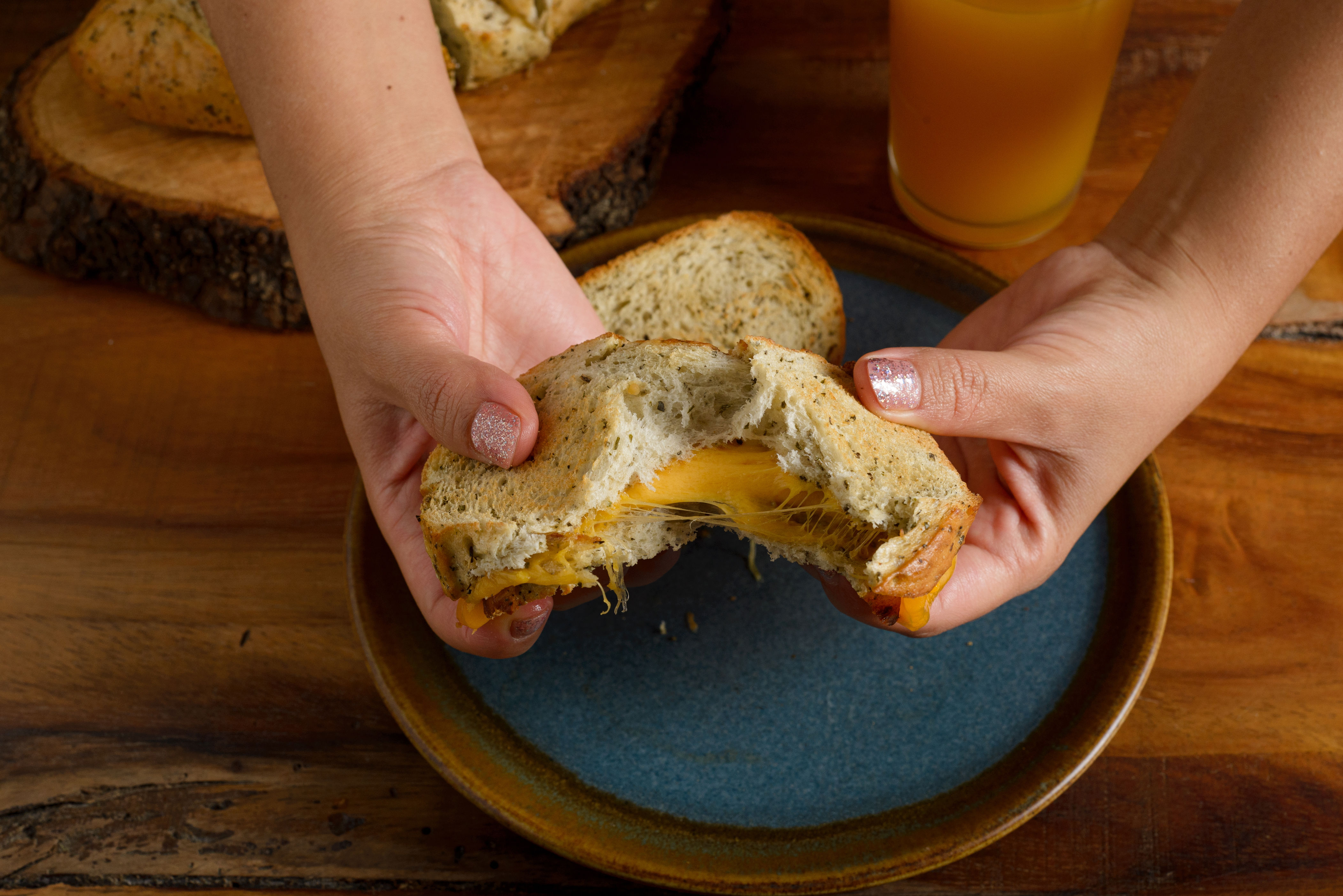 Hands breaking apart a grilled cheese sandwich on a plate, with juice in the background