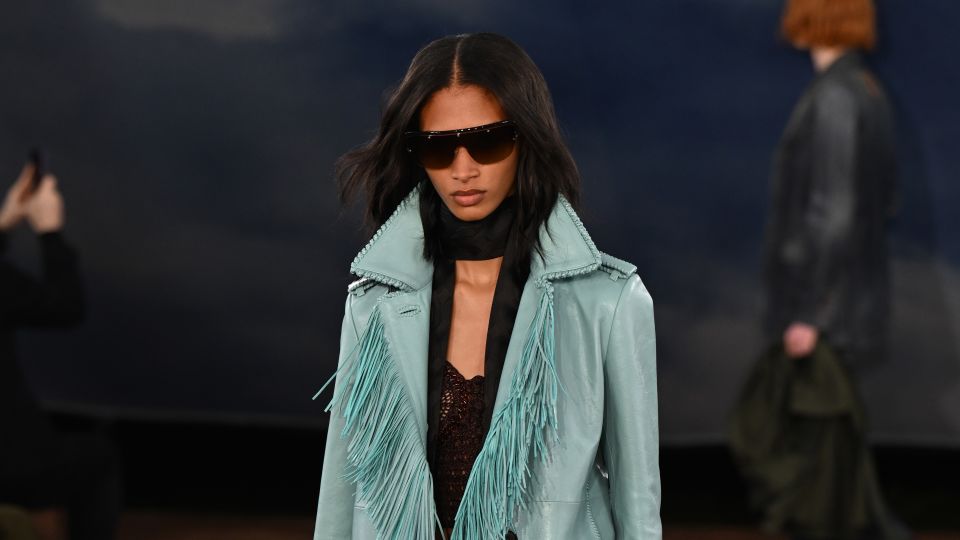 Model walking the runway in a festival-worthy fringed aqua blue leather coat