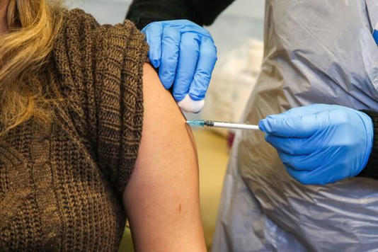 A National Health Service (NHS) staff member administers a...