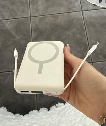 A person holds a MagSafe-compatible power bank with attached USB-C cables, suitable for charging devices on the go