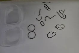 Assorted shapes and symbols are drawn on a white surface next to a measuring tape and two transparent square containers