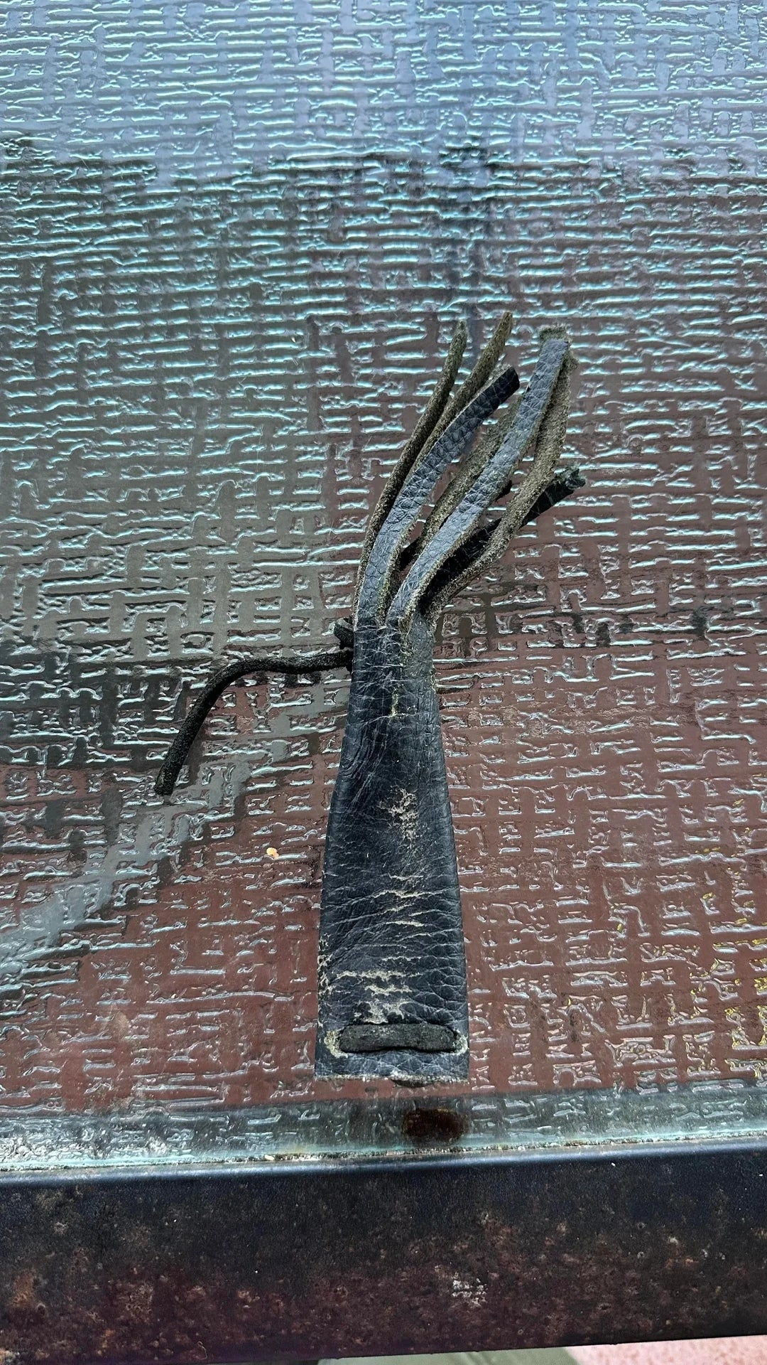 Frayed, worn black leather piece with multiple split ends, lying on a textured glass table surface