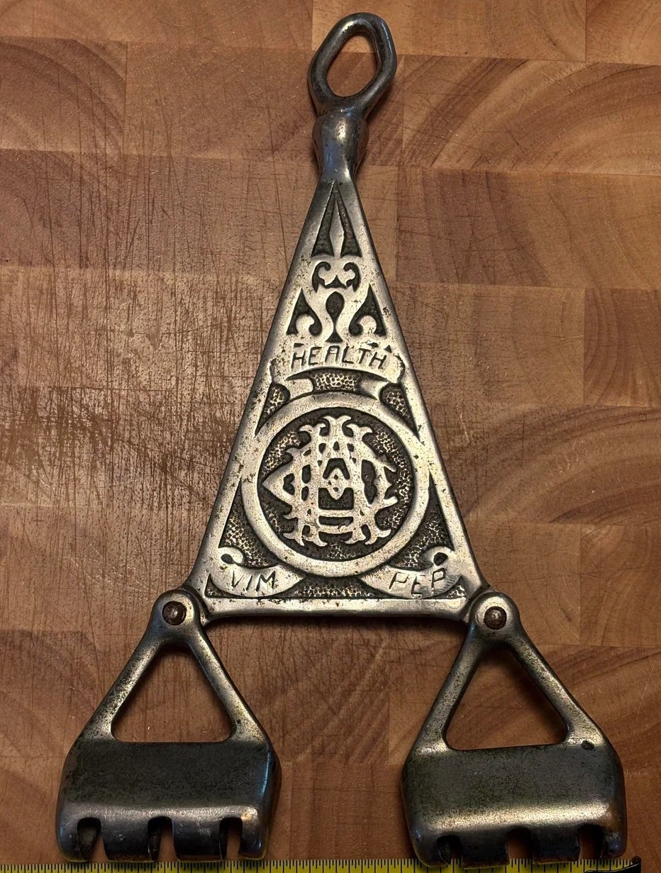 Metal object with ornate design and phrase "Health" engraved; ruler below for scale. Appears vintage or traditional