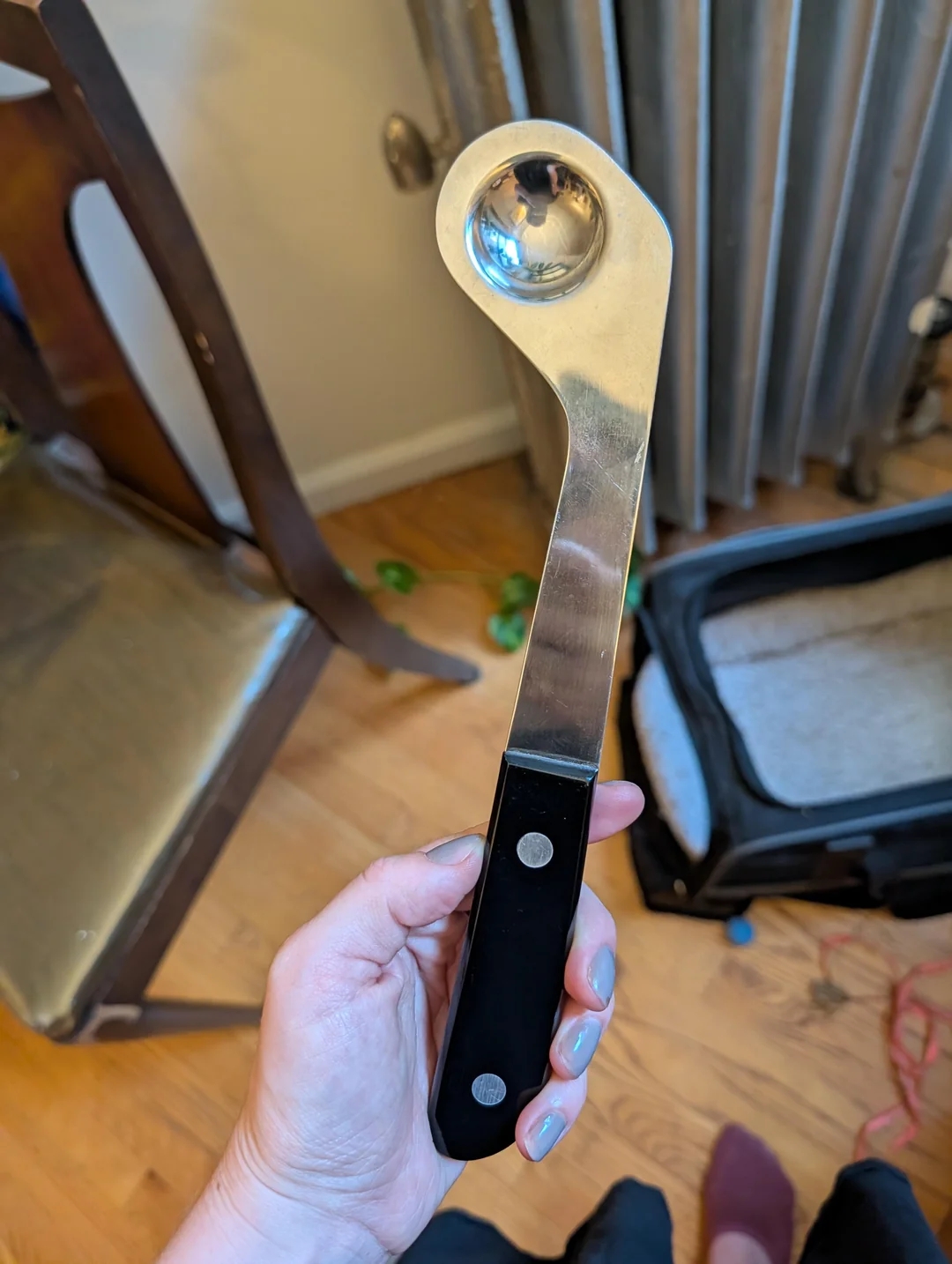 Person holding an unusual metal utensil with a curved handle and a round bowl, possibly a unique kitchen tool or crafting implement