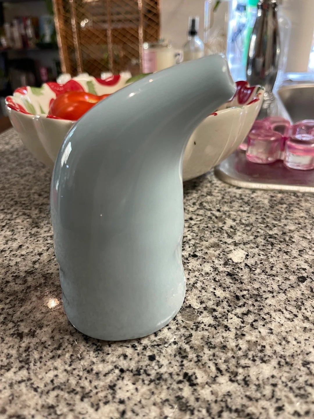 Unusual blue ceramic object on a kitchen counter with fruit bowl and candles in the background