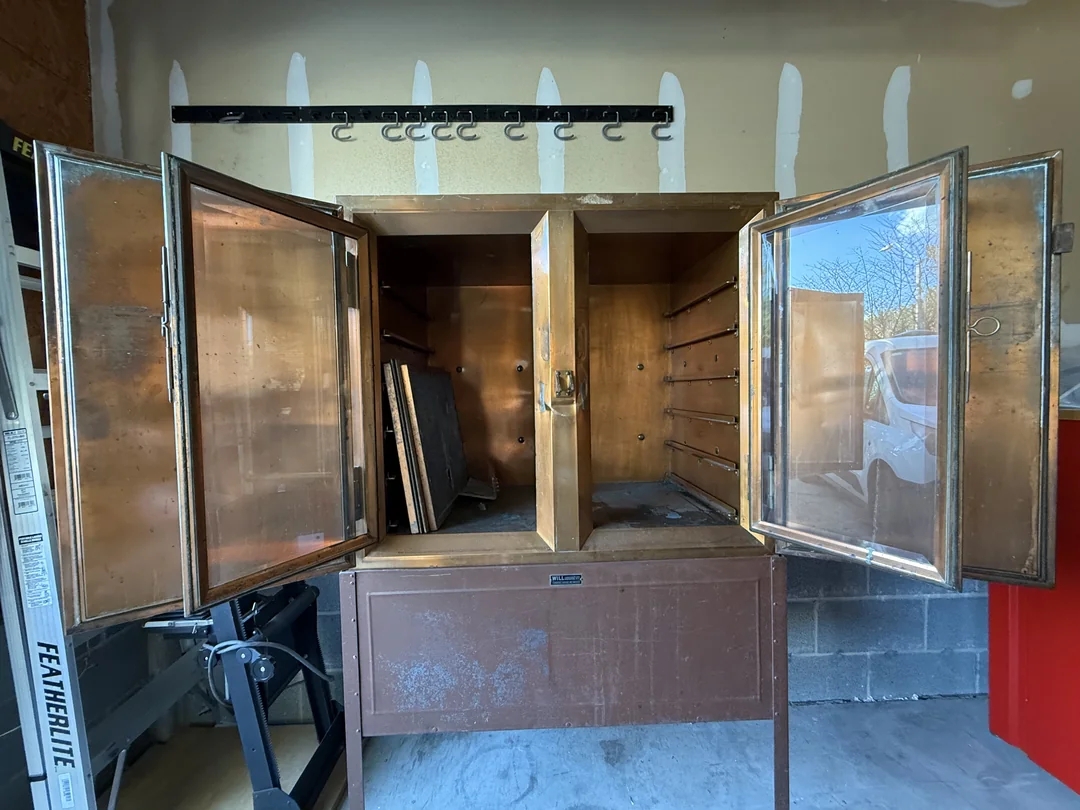 Open metal cabinet in a garage, showing shelves and hooks. Sides are open, with visible storage space and empty areas
