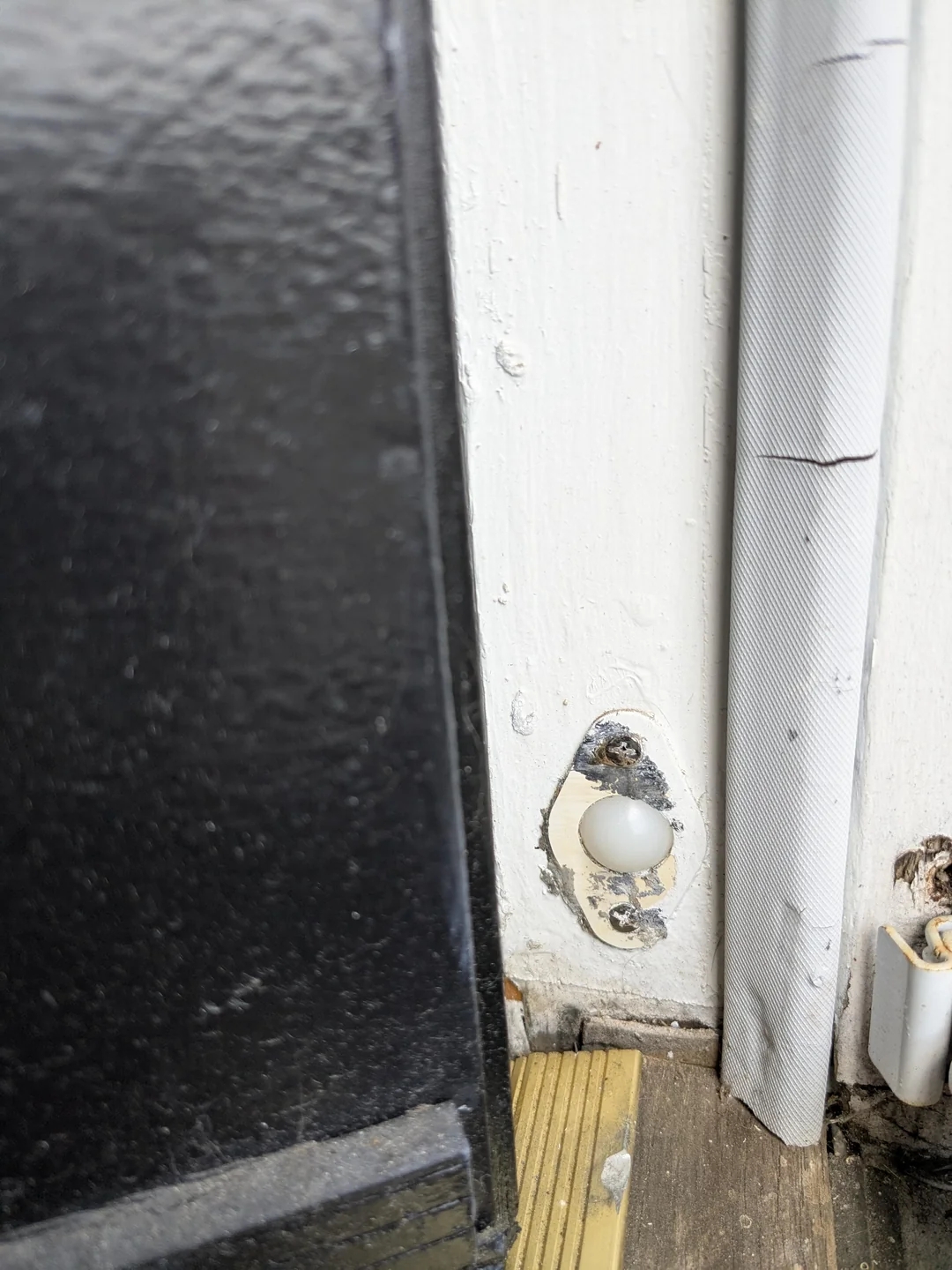 Doorbell without a cover with exposed wires and a bulb, mounted on a wooden surface beside a door frame