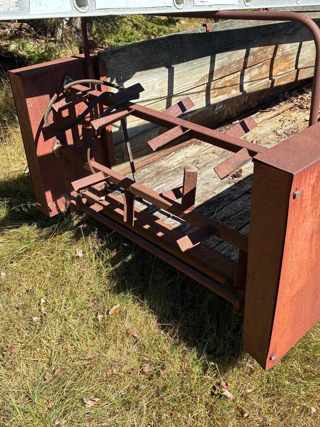 Rusty, old farming equipment with metal parts, set on grass, possibly for hay or grain collection