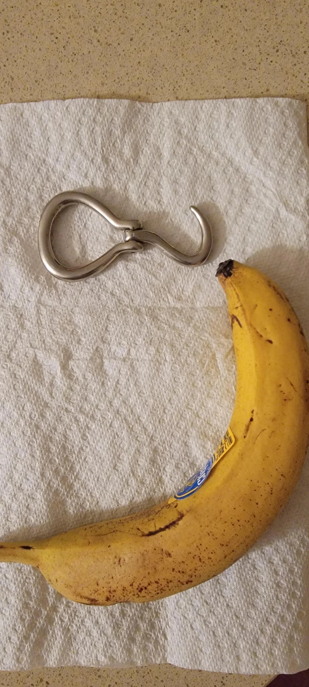 Banana with a metal hook resembling a teardrop or fishhook shape, resting on a white paper towel