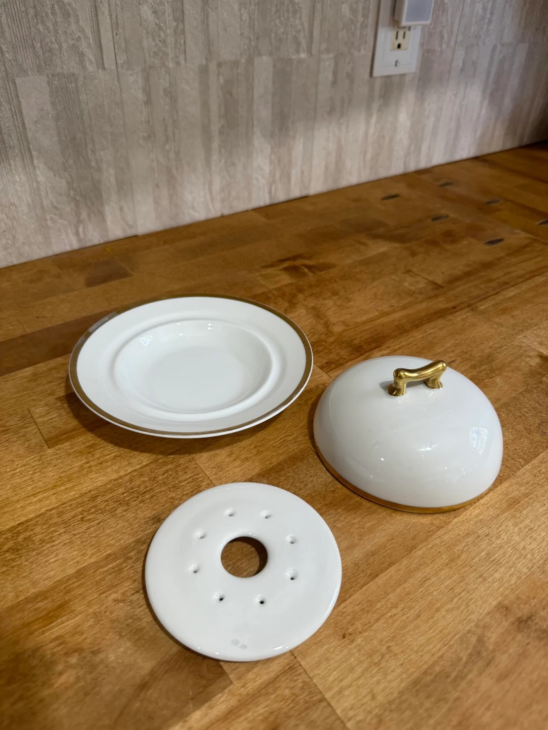 Ceramic butter dish with lid, plate, and perforated insert on a wooden countertop