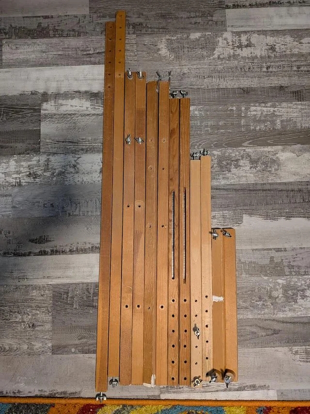Stacked wooden bed slats with various holes and hardware lying on a patterned floor, resembling a city skyline