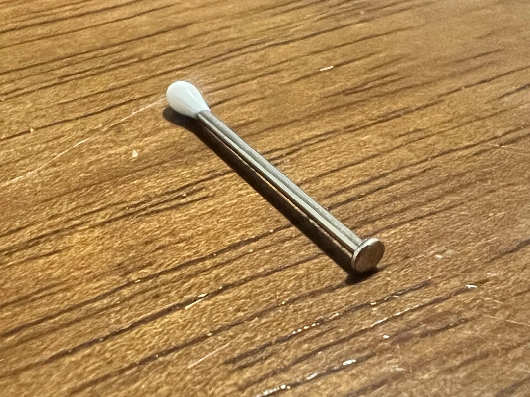 Small metal rod with a rounded white tip, lying on a wooden surface