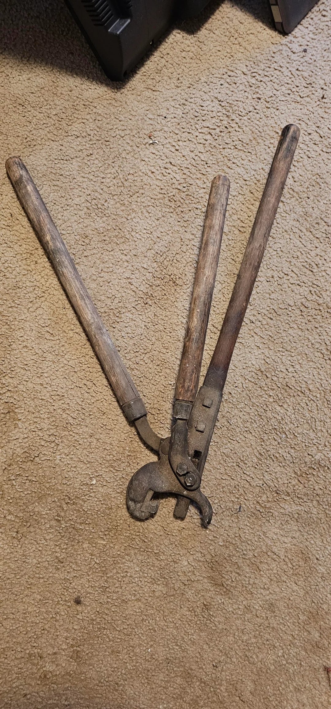 Two old, wooden-handled tools with metal heads, possibly vintage farm equipment, resting on a carpeted floor