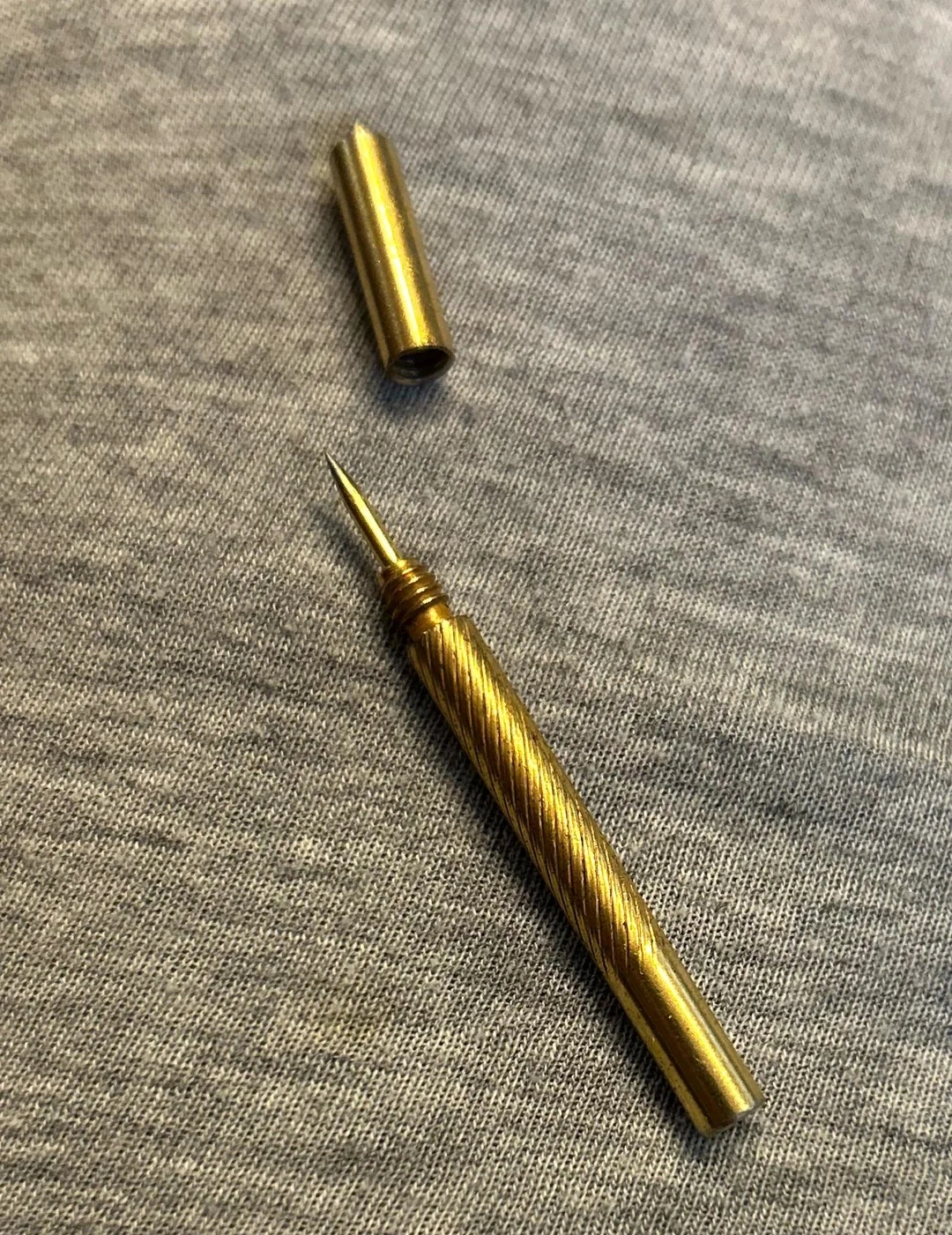 A small, ornate brass needle holder with a screw-on cap, displayed open on a fabric surface