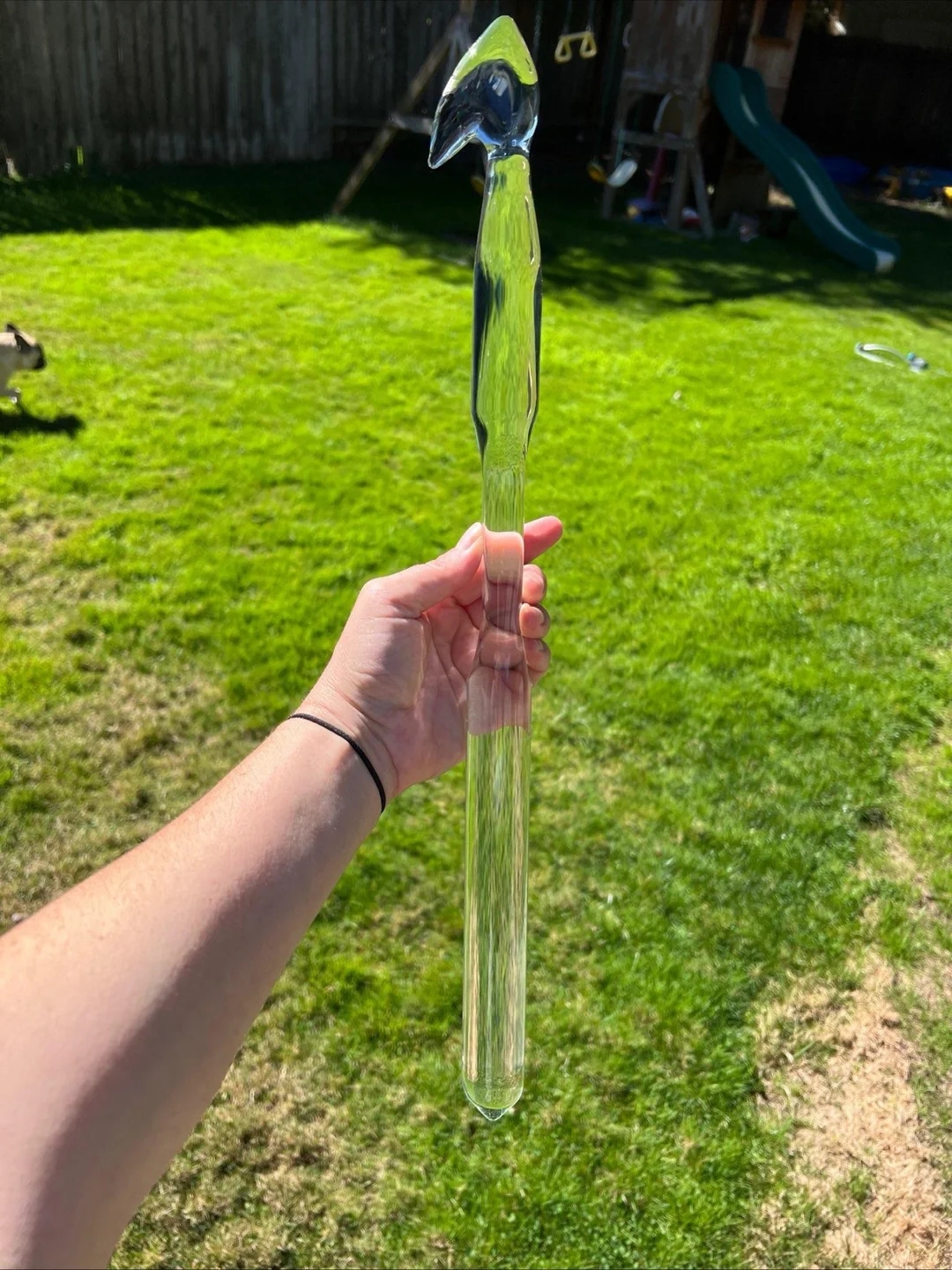 A hand holds a clear, uniquely shaped glass object resembling a bird, in an outdoor grassy setting