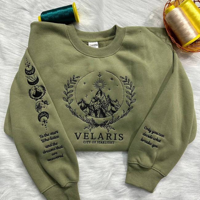 Green sweatshirt featuring mountain design with celestial symbols, inspirational text about dreams and resilience, and the word