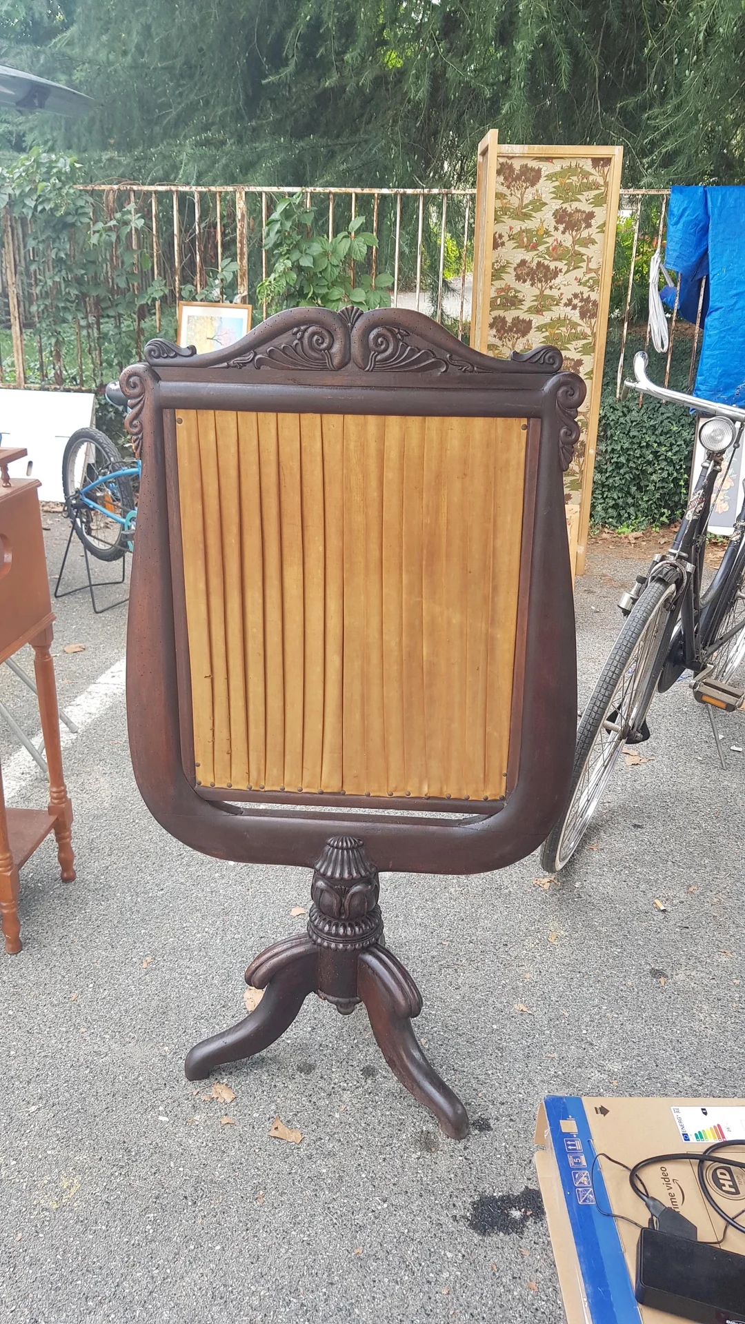 Decorative wooden stand with ornate carvings and slatted middle, displayed at an outdoor market next to a bicycle and other items