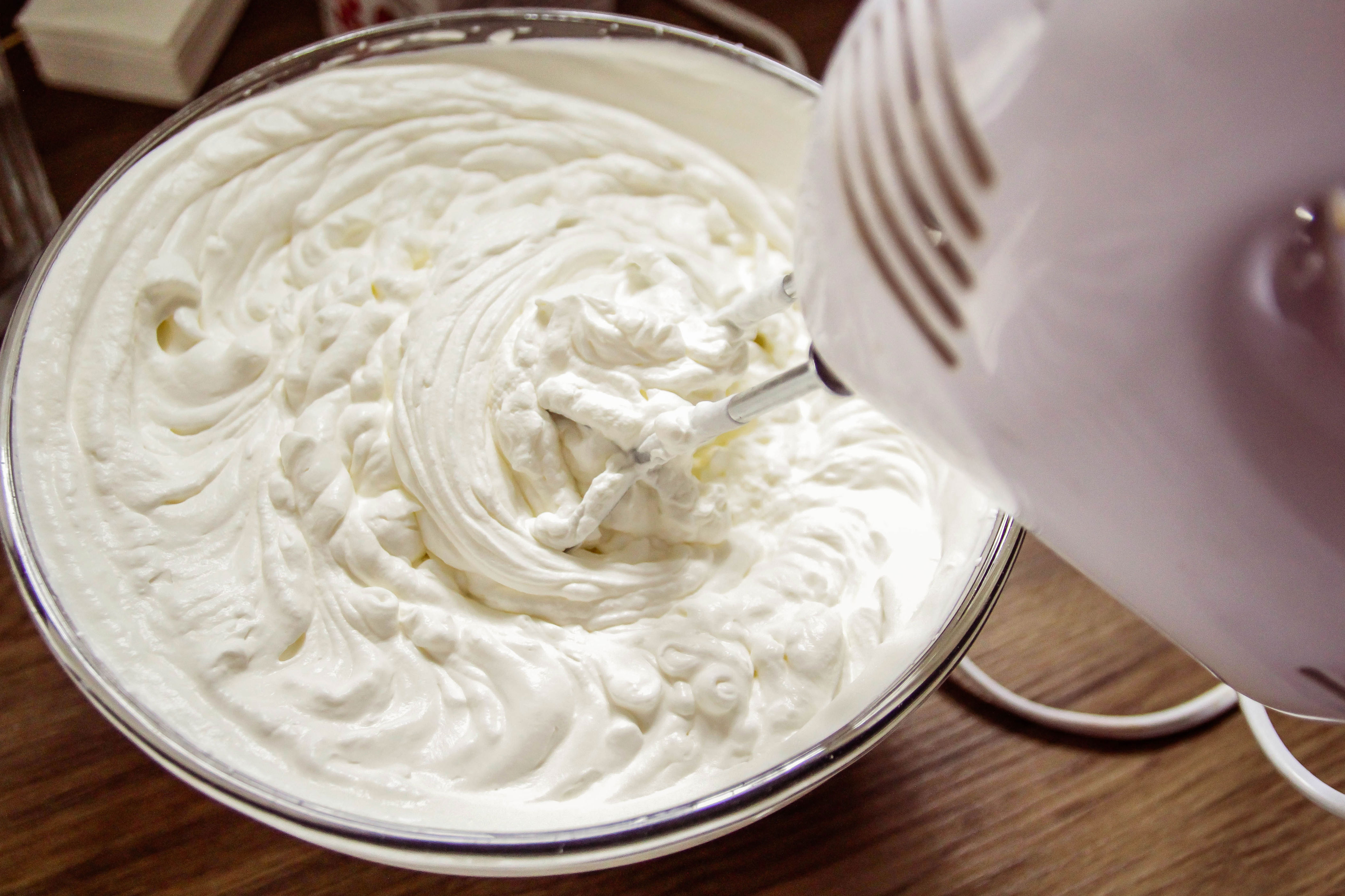 Electric mixer whipping cream in a glass bowl on a wooden surface