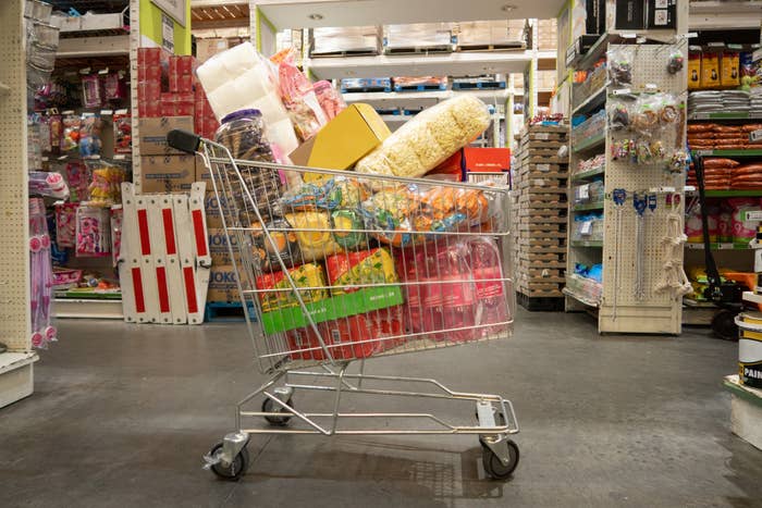 Shopping cart filled with bulk snacks and household items in a warehouse store aisle