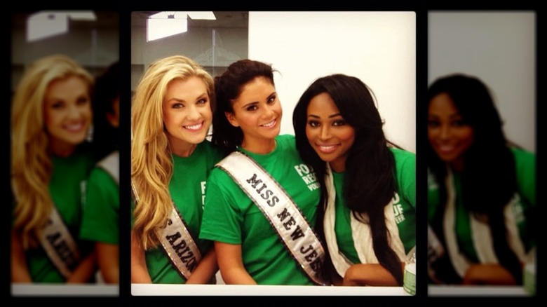 Erika Kirk wearing a green shirt and sash, posing beside two other women.