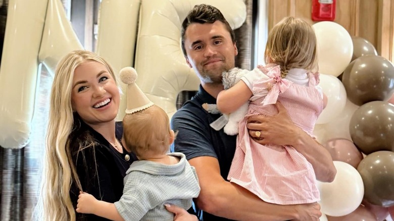 Erika Kirk smiling holding her son with her husband Charlie Kirk holding their daughter.