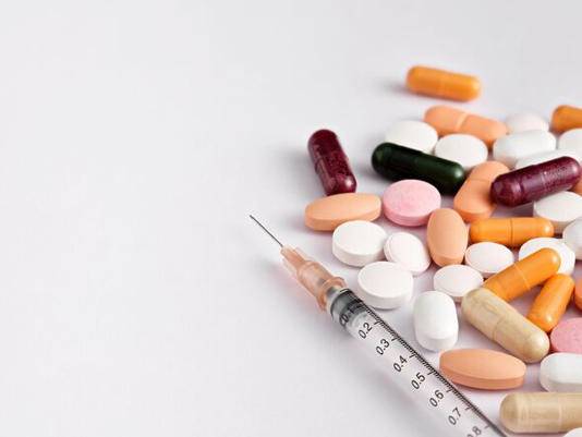 Syringe and colorful pills forming a background for pharmaceutical concept