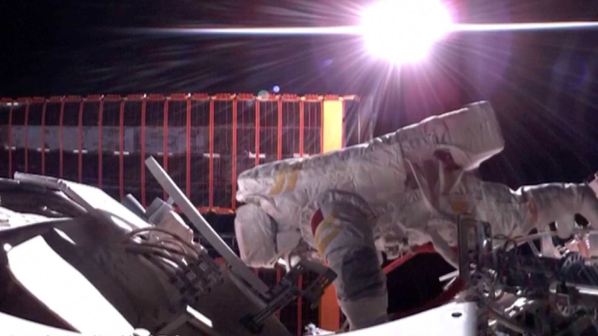 an astronaut in a white spacesuit spacewalks outside a space station with the bright sun in the background