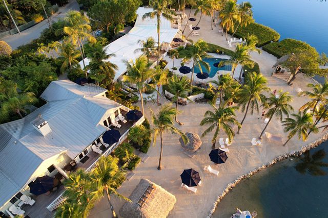 Aerial view of a resort area with villas palm trees a pool lounge areas and a waterfront setting