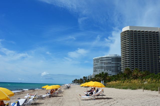 Beach with yellow umbrellas and modern buildings in the background people relaxing on lounge chairs near the shore