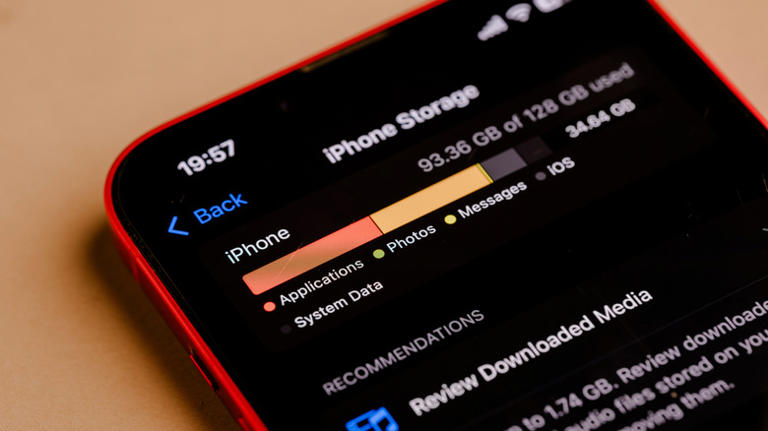 An iPhone laying on an orange backdrop displaying its available storage space from the Settings screen