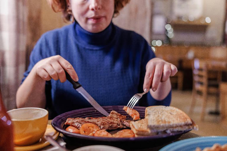 Unrecognizable woman hands slicing meat dish on a plate in a bright restaurant