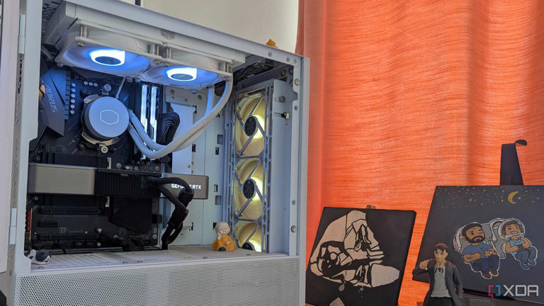 A white gaming PC with RGB fans next to a curtain and some paintings