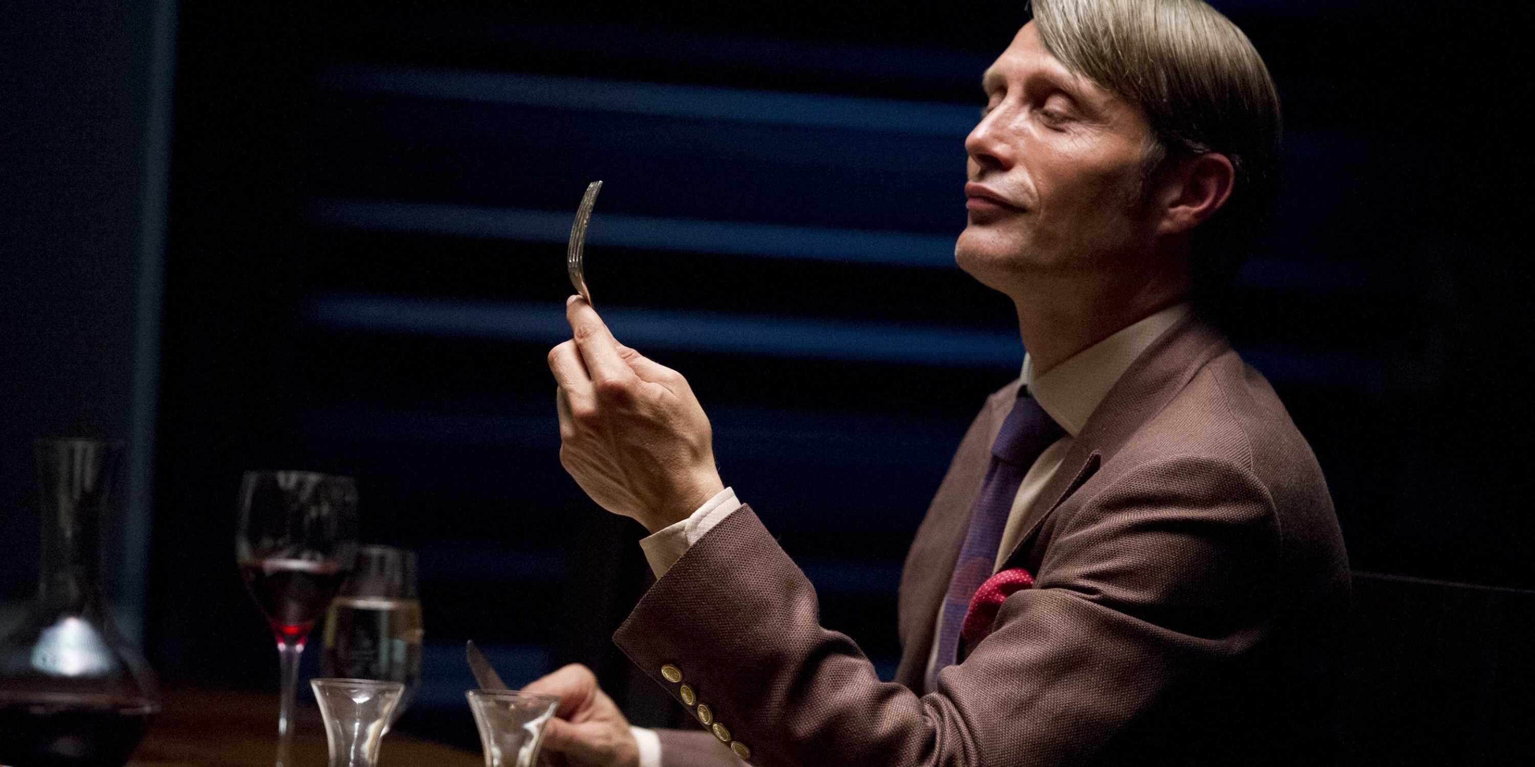 Hannibal Lecter (Mads Mikkelsen) examining a fork at a dining table in Hannibal season 1 episode 1
