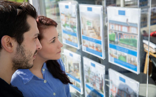 Couple looking at house prices in estate agent's window
