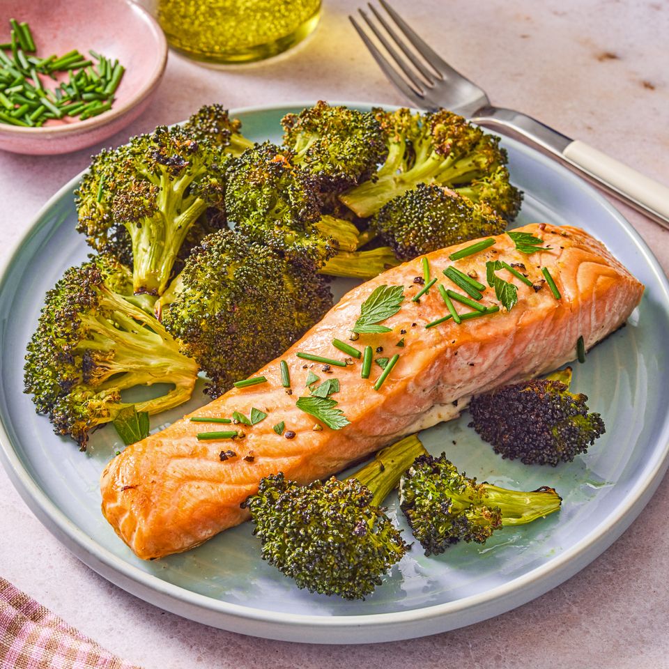 A plate of baked salmon topped with herbs served alongside roasted broccoli