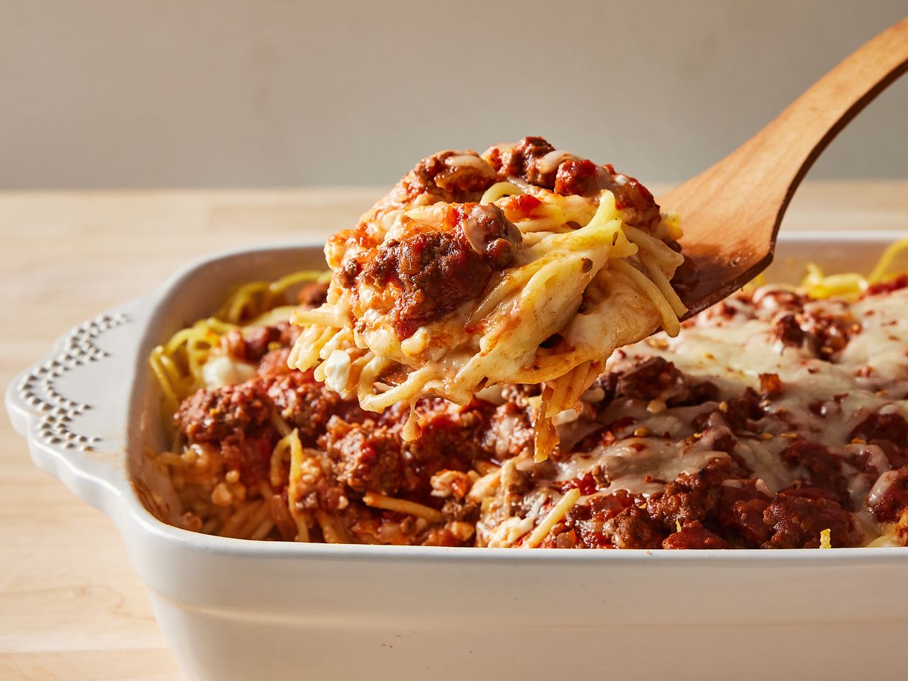 Baked spaghetti in a dish being served with a wooden spoon