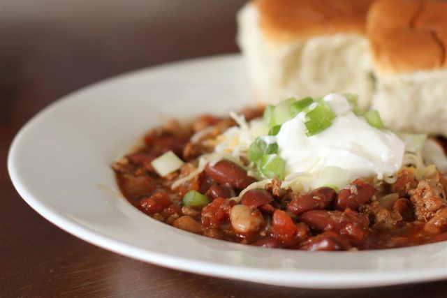 a bowl of Simple Turkey Chili topped with sour cream and green onions and cheese with two rolls on the bowl rim