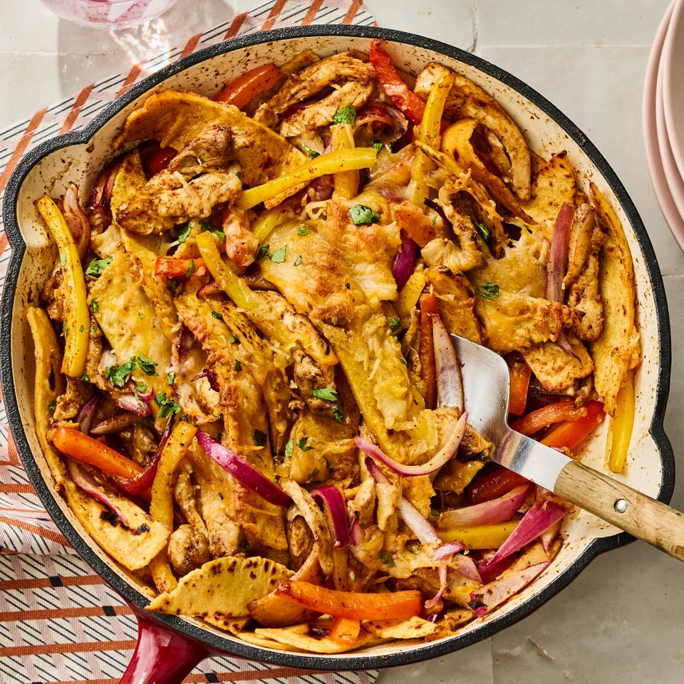 A skillet containing chicken fajita casserole with cooked vegetables and melted cheese served with a spatula