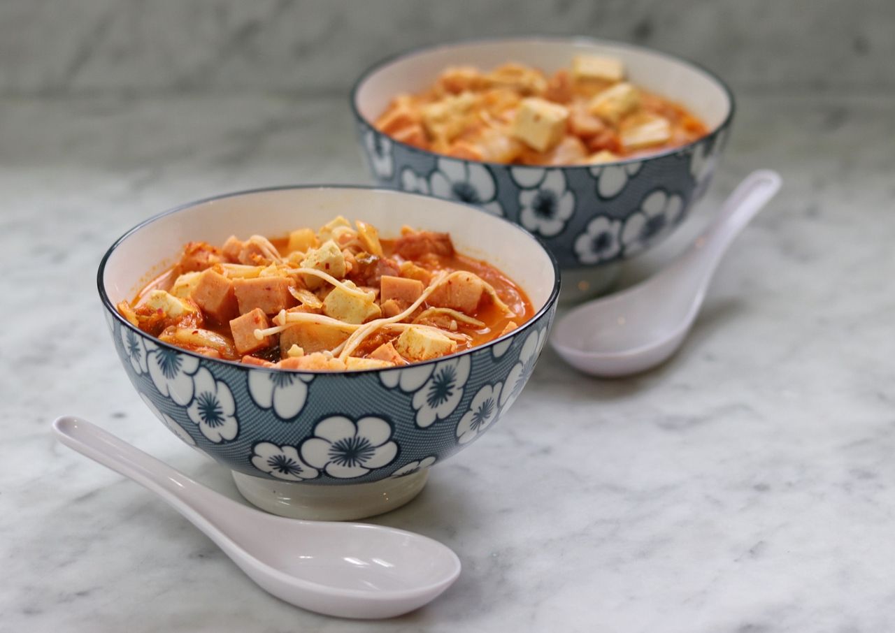 Two bowls of tofu soup placed on a marble surface blue floralpatterned bowls and white spoons alongside the bowls