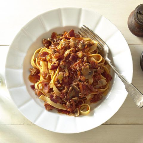 close up view of Bolognese Sauce with pasta in a white bowl, with a fork