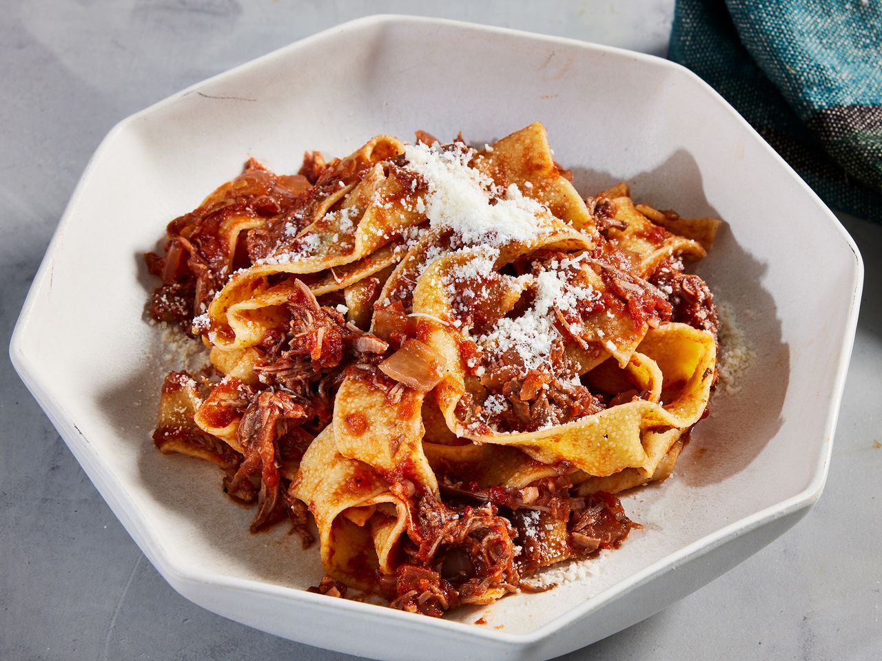 A bowl of pasta topped with shredded beef ragu and grated cheese