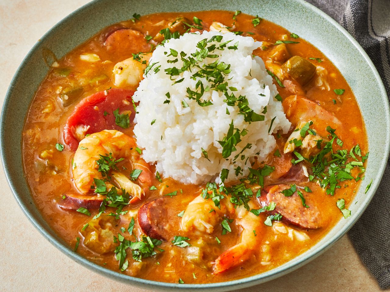 a close up view of a single bowl of creole gumbo served with steamed white rice and fresh herbs