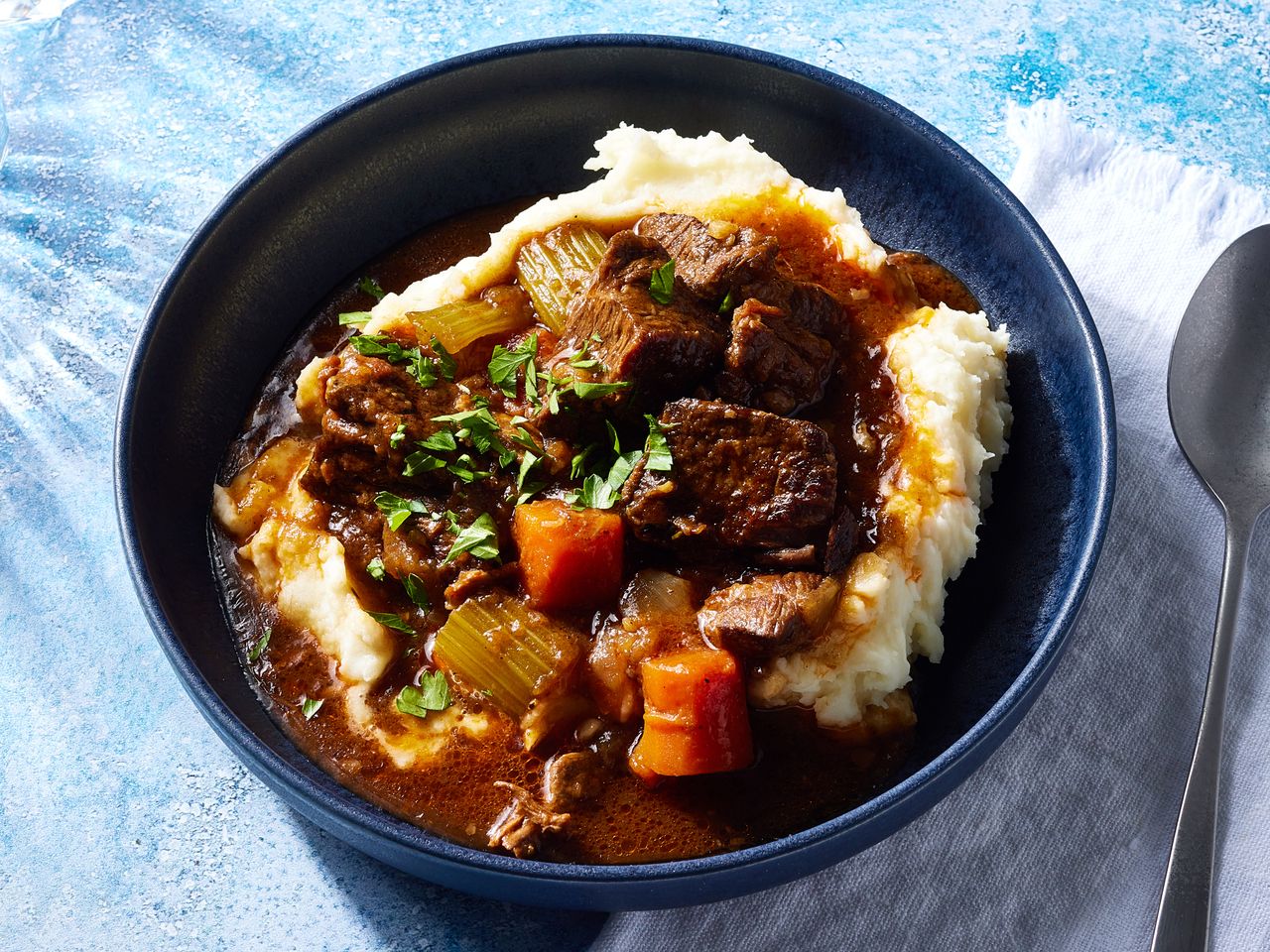 A bowl of beef and Guinness stew, served over mashed potatoes and garnished with chopped parsley